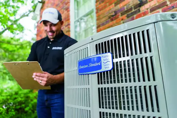 HVAC technician with clipboard standing next to an American Standard AC unit